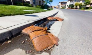 Stormwater design shown through a curb inlet with sandbags and surface runoff on a residential street during rain preparedness.