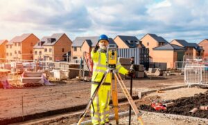 Surveyor using total station to measure property survey data near residential homes in a flood zone