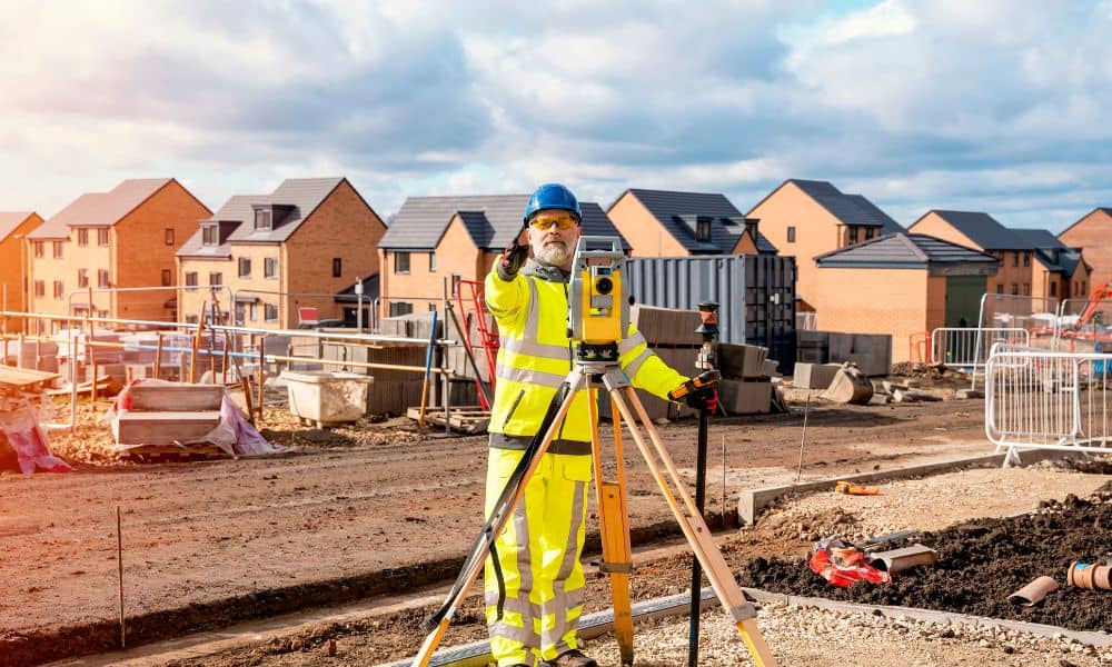 Surveyor using total station to measure property survey data near residential homes in a flood zone
