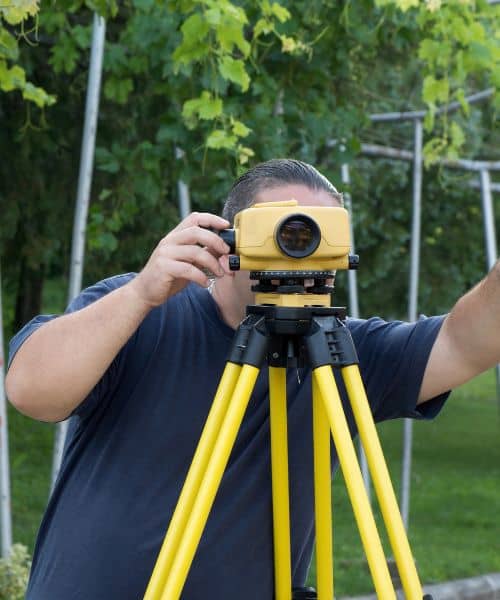 Surveyor using equipment to perform a flood elevation survey on residential land