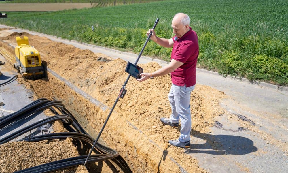 Construction surveyor measuring trench depth and site layout before excavation
