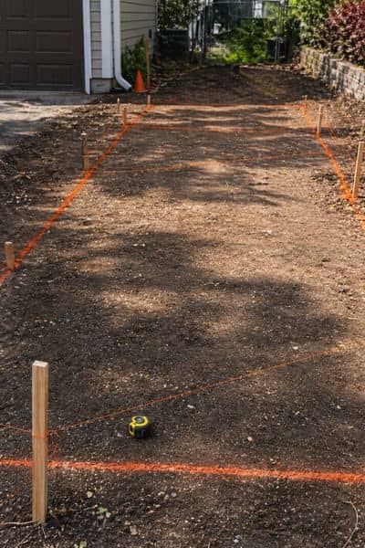A local surveyor marking driveway layout with stakes and string lines to guide accurate concrete placement