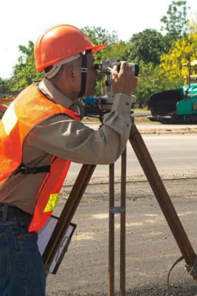 Construction surveyor checking site layout near roadwork with equipment set up on site